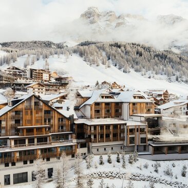 Aman Rosa Alpina exterior with snow-covered Dolomite peaks and Alpine village landscape in winter.