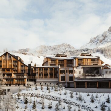 Aman Rosa Alpina exterior with snow-covered Alpine peaks and forested slopes in winter.