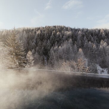 Steaming outdoor pool at Aman Rosa Alpina with snow-covered forest and misty mountains beyond.