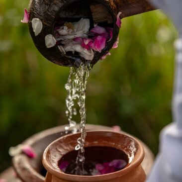 Water being poured into a wooden bowl with rose petals at Amanjiwo's wellness sanctuary.
