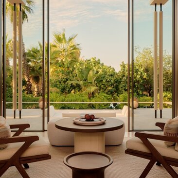 Living area at Amanvari with expansive windows overlooking estuary gardens and tall palms.
