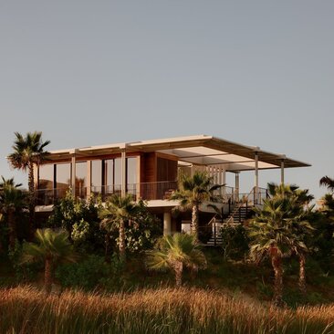 Amanvari casita with extended canopy sheltering the structure, surrounded by desert landscape and palm trees at golden hour.