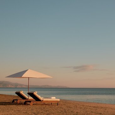 Two sun loungers and a parasol on Amanvari's beach at sunset.
