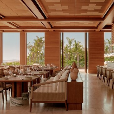 Amanvari's dining venue with warm wood interiors, large windows overlooking desert landscape, and contemporary furnishings.