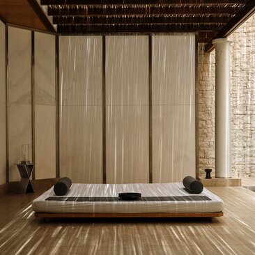 Spa treatment room at Amanzoe with wooden platform bed, draped curtains, and stone walls.