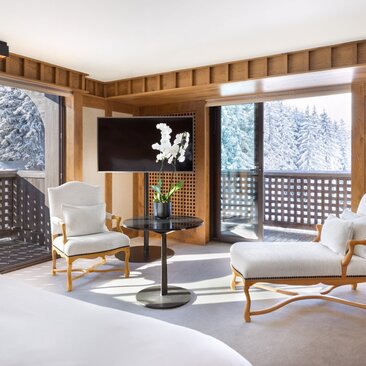 Wooden-panelled bedroom at Aman Le Mélézin with dual seating areas and snow-view windows.