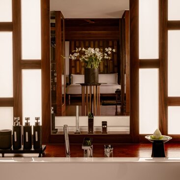 Amanpuri pavilion bathroom vanity with wooden cabinetry, candles, and floral arrangement reflected in mirror.