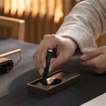 Hands practising calligraphy with brush and ink at Nanshufang Calligraphy Room, Aman New York.