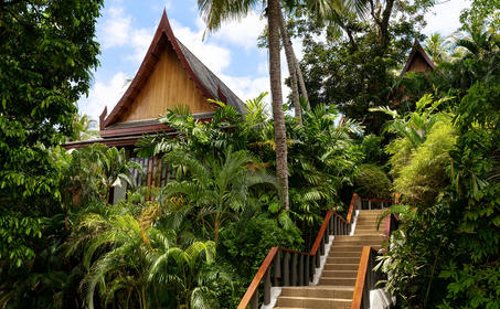 安缦璞瑞度假村的海景阁楼，木质阶梯通往传统泰式尖顶建筑，四周被郁郁葱葱的热带植被环绕。