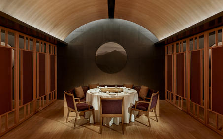 养云安缦度假村的餐厅，拱形天花板下摆放着圆形餐桌和木制椅子。