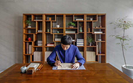 养云安缦度假村内，一位身穿蓝色衣服的人坐在木制书架前的书桌处。