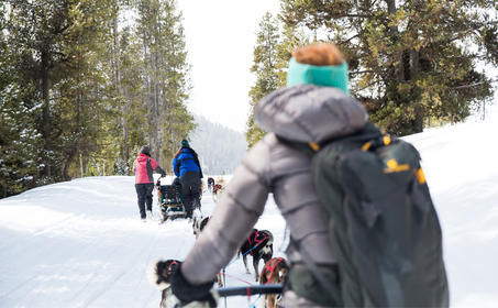 Child in colourful winter hat sitting on snow sculpture at Amangani, with guests walking in snowy landscape behind.