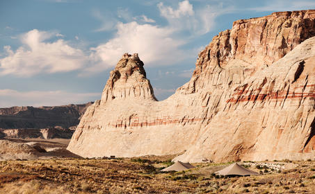 Rock formations rise from the desert landscape at Amangiri, Utah, beneath a partly cloudy sky.