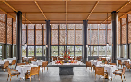 养云安缦度假村的宽敞餐厅，木质梁柱与落地窗框构成现代设计，餐桌整洁排列。