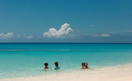 一家人在安缦涯澜度假村的浅蓝色海水中嬉水,白沙滩在前。