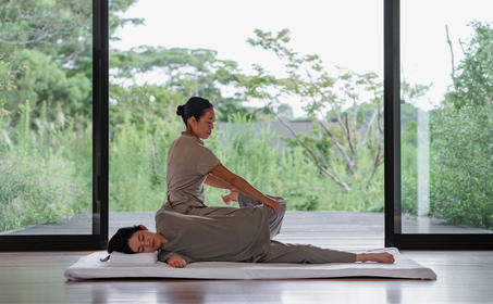 Wellness instructor leading a guided meditation session at Amanemu, with expansive garden views beyond the floor-to-ceiling windows.