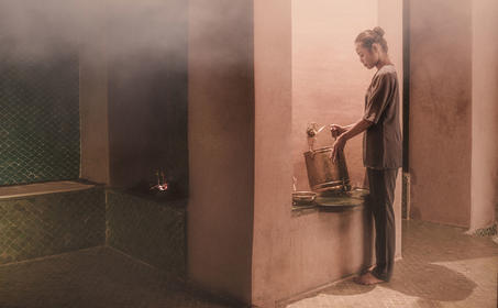 Spa attendant standing in a softly lit corridor at Amanjena resort wellness centre.