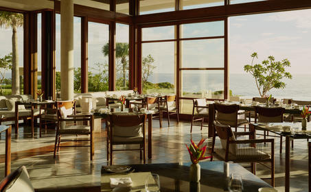 Amanera's main dining venue with floor-to-ceiling windows overlooking the landscape, wooden tables and chairs, and natural light.