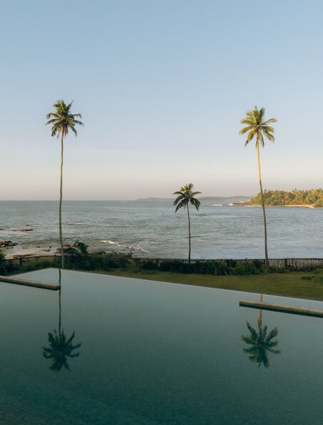 Infinity pool overlooking the Indian Ocean at Amanwella, Sri Lanka, with palm trees reflected in still water.