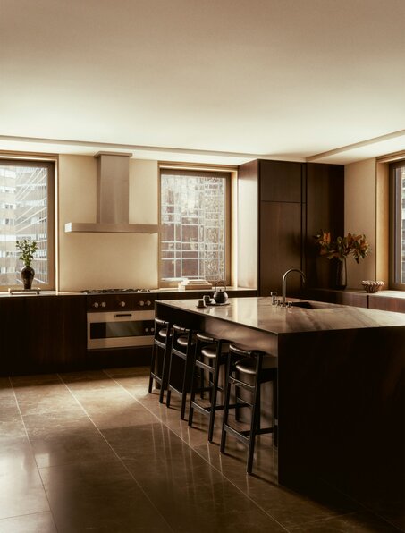 Penthouse kitchen with warm wood cabinetry, bar seating, and floor-to-ceiling windows at Aman New York.