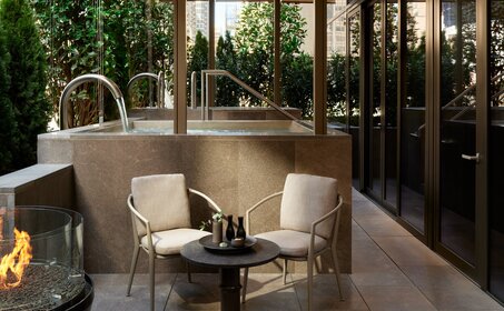 Terrasse du spa Aman New York avec fauteuils crème, foyer et verdure.