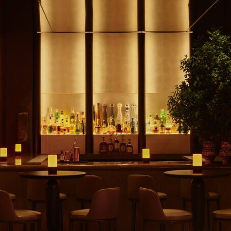 Candlelit jazz club bar at Aman New York hotel, with warm amber lighting and floor-to-ceiling windows.