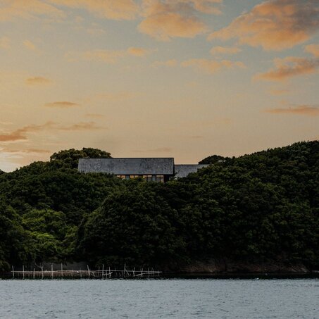 Amanemu's modern architecture positioned on a forested hillside at sunset, overlooking calm waters.