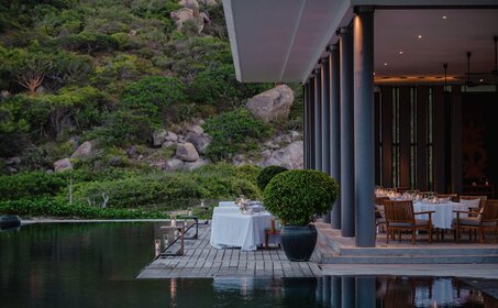 安缦诺怡度假村海滩俱乐部餐厅外，白色躺椅靠近无边际泳池，背景为现代建筑。