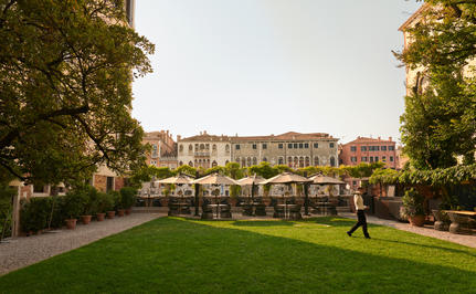 Manicured garden at Aman Venice with palazzo beyond, bordered by tall hedges and mature trees.