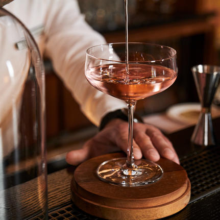 Bartender pouring a cocktail into a coupe glass at Aman Venice's bar.