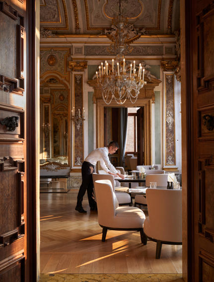 The Ballroom at Aman Venice, with parquet flooring, ornate wooden panelling, crystal chandelier and period furnishings.