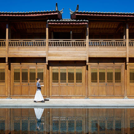 大研安缦度假村内，一位身着白色服装的访客坐在反射池前，背景为传统木制建筑。