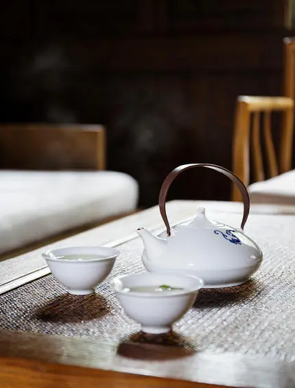 Teapot and cups arranged on white cloth at Amanfayun, with wooden chairs in background.