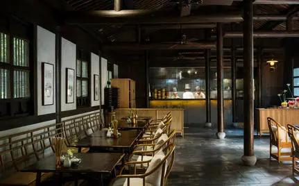 Amanfayun's dining venue with wooden tables and chairs, framed artworks on walls, and warm overhead lighting.