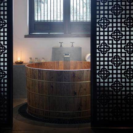 木制浴桶置于法云安缦度假村浴室内，两侧饰以黑色镂空屏风。