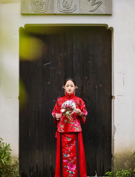 Woman in red traditional áo dài standing before dark wooden door at Amanfayun.
