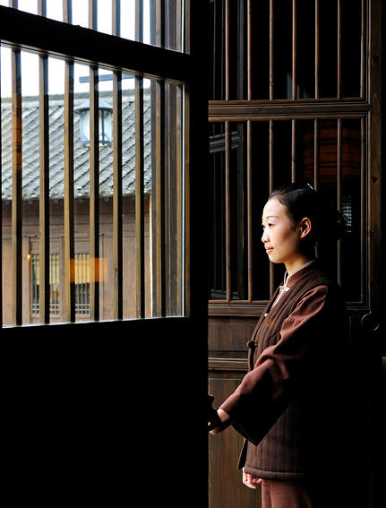 法云安缦度假村内，一位访客站在传统木制门框旁，透过竖条纹窗户向外眺望。