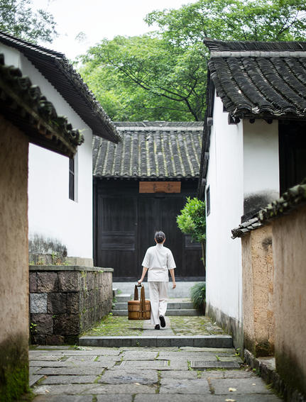 法云安缦度假村的白墙黑瓦走廊，一位访客漫步其中，两侧传统建筑环绕。