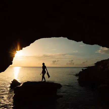 Silhouetted figure walking through a rocky cave opening at sunrise, Amanyara resort.