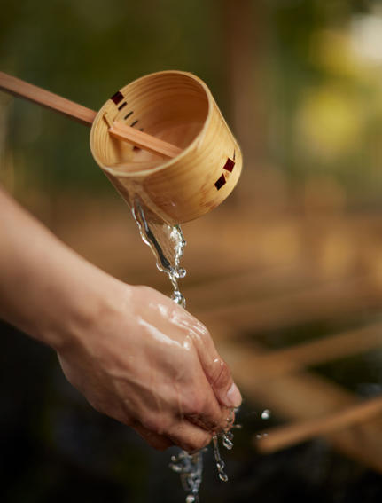 Water pours from a wooden dipper into an open hand at Amanemu resort.