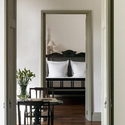 View through doorway to Amangalla bedroom with framed mirror and fresh flowers on side table.