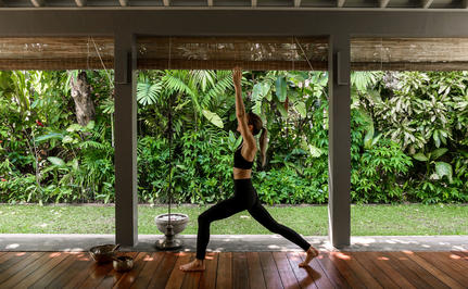 Woman in yoga pose on mat within covered pavilion at Amangalla, lush garden visible beyond.