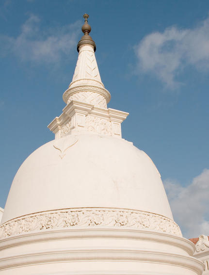White domed stupa with ornate detailing under blue sky at Amangalla.