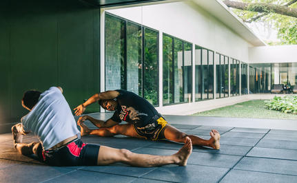 Yoga mat and props arranged on a stone terrace at Amansara, with green walls and glass doors beyond.