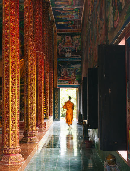 Monk walking through illuminated temple corridor at Amansara, Cambodia.