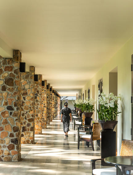 Colonnade with stone pillars at Amansara, dappled light creating shadows along the covered walkway.