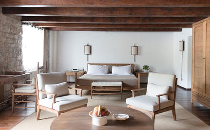 Deluxe cottage bedroom at Aman Sveti Stefan with wooden beams, neutral furnishings, and seated area overlooking Montenegro's coast.