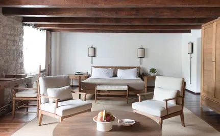Deluxe cottage bedroom at Aman Sveti Stefan with wooden beams, neutral furnishings, and seated area overlooking Montenegro's coast.