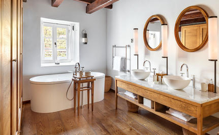 Deluxe cottage bathroom at Aman Sveti Stefan with freestanding tub, wooden vanity and woven mirrors.