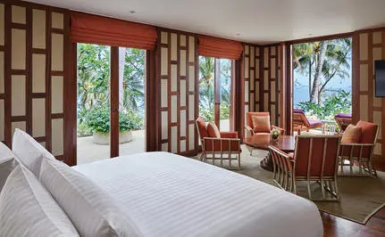 Principal bedroom at Amanpuri resort with ocean views through wooden-framed doors opening to a terrace.